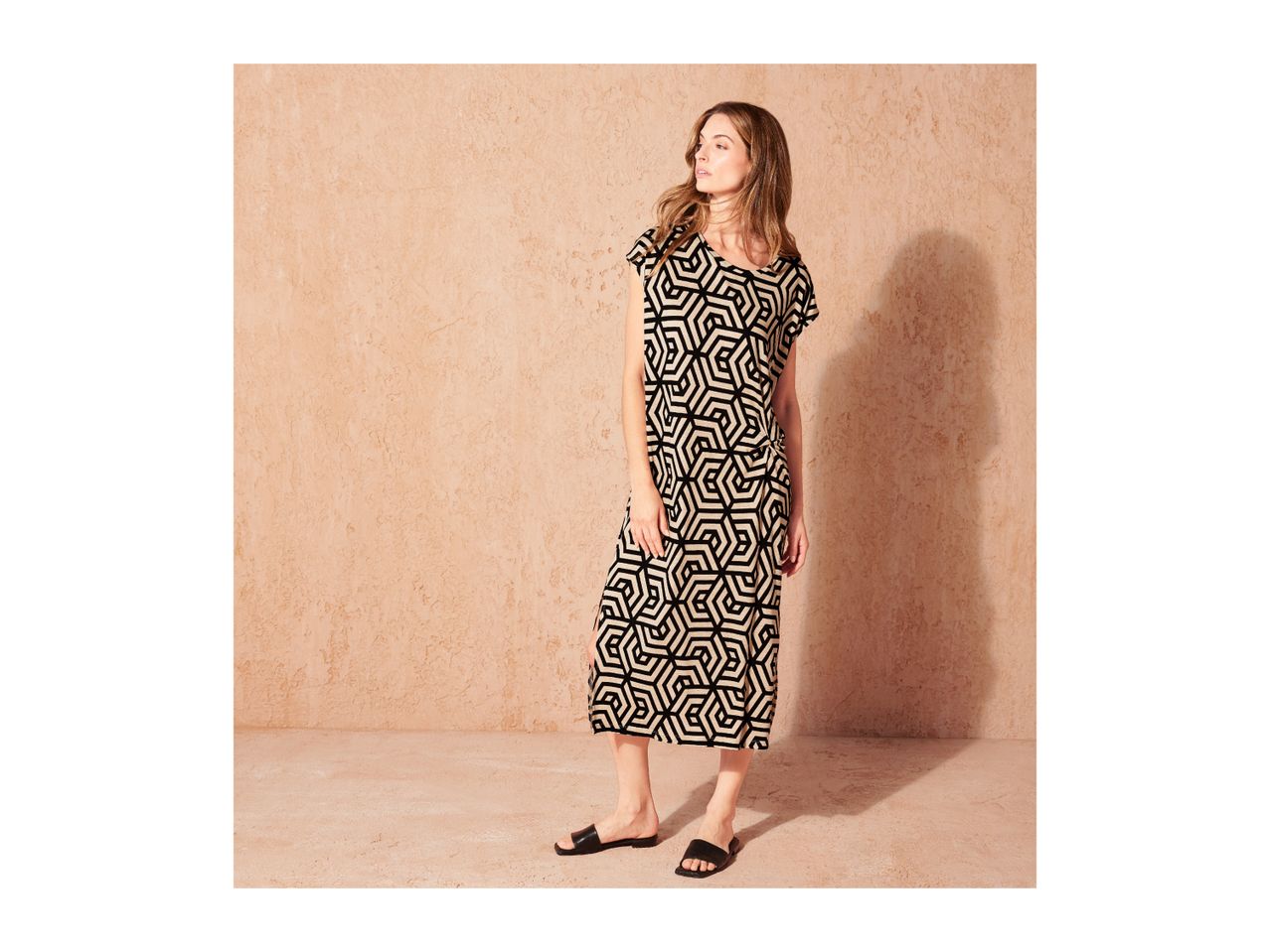 Woman in a black and beige geometric print midi dress and black sandals.