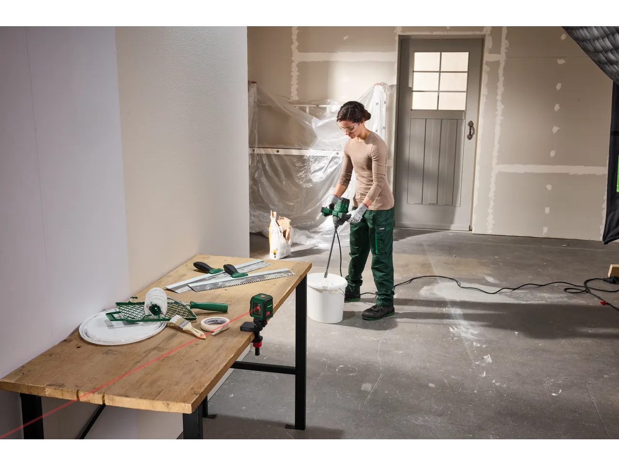 Woman mixing paint with a PARKSIDE® mixer, with a PARKSIDE® Cross Line Laser on a table.
