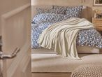 Un letto con lenzuola blu a fantasia floreale e un plaid beige chiaro.