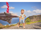 Criança pequena com t-shirt Lupilu com padrão de dinossauros e calções de ganga, a brincar ao ar livre.