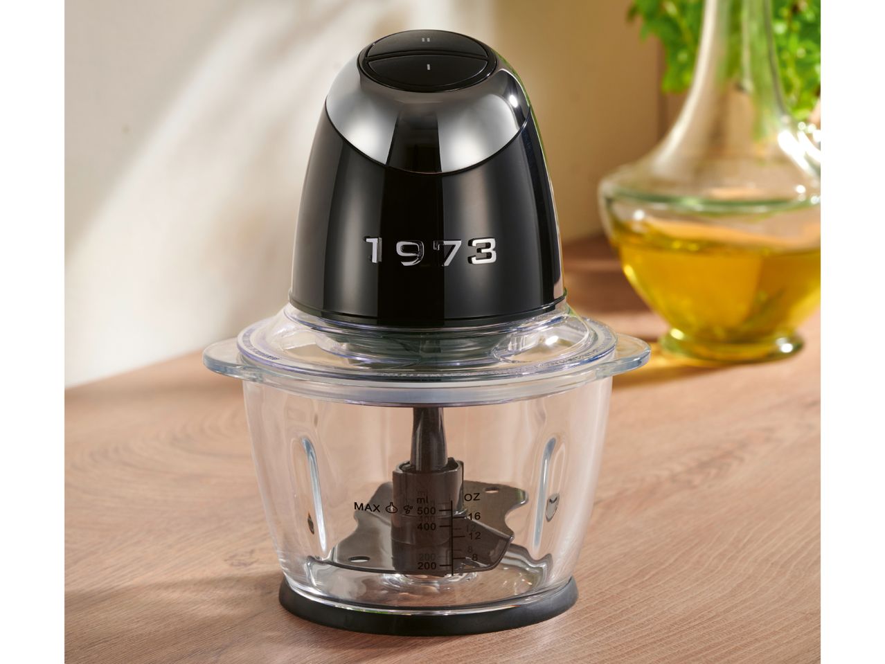 A black and chrome food chopper with a clear bowl on a wooden surface.