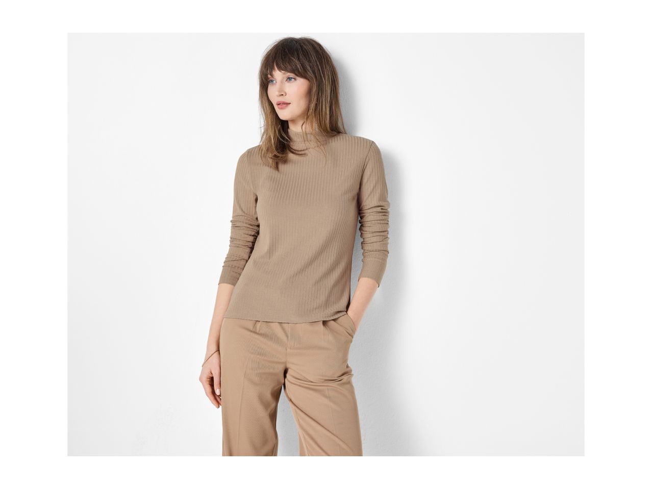 Woman in a beige ribbed long-sleeve top and matching trousers, hands in pockets, looking left.