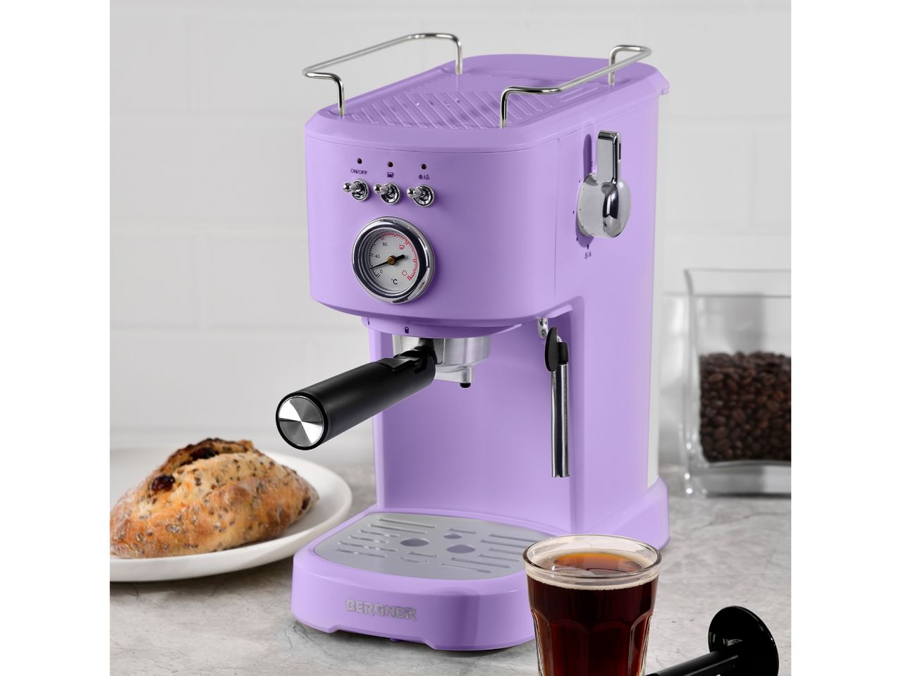 A lavender-colored retro-style espresso machine sits on a countertop next to a pastry and a cup of coffee.