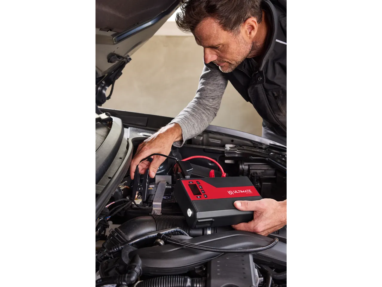 Um homem usa um arrancador portátil ULTIMATE SPEED para ligar um carro.