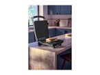 A panini press with a grilled sandwich on a wooden kitchen counter.