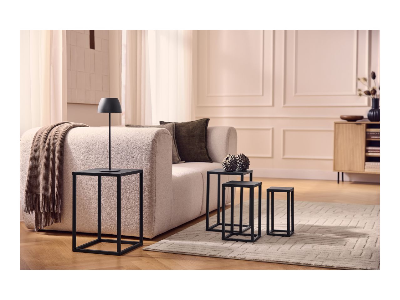 Modern living room with a beige sofa, black side tables, a lamp, and a textured rug.