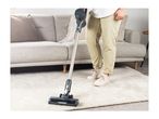 Person vacuuming a light-colored rug in a living room with a cordless stick vacuum.