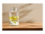 Glass beverage dispenser with lime slices and ice cubes on a wooden surface.
