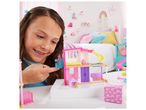 Une jeune fille joue avec une maison de poupée Barbie rose et colorée.