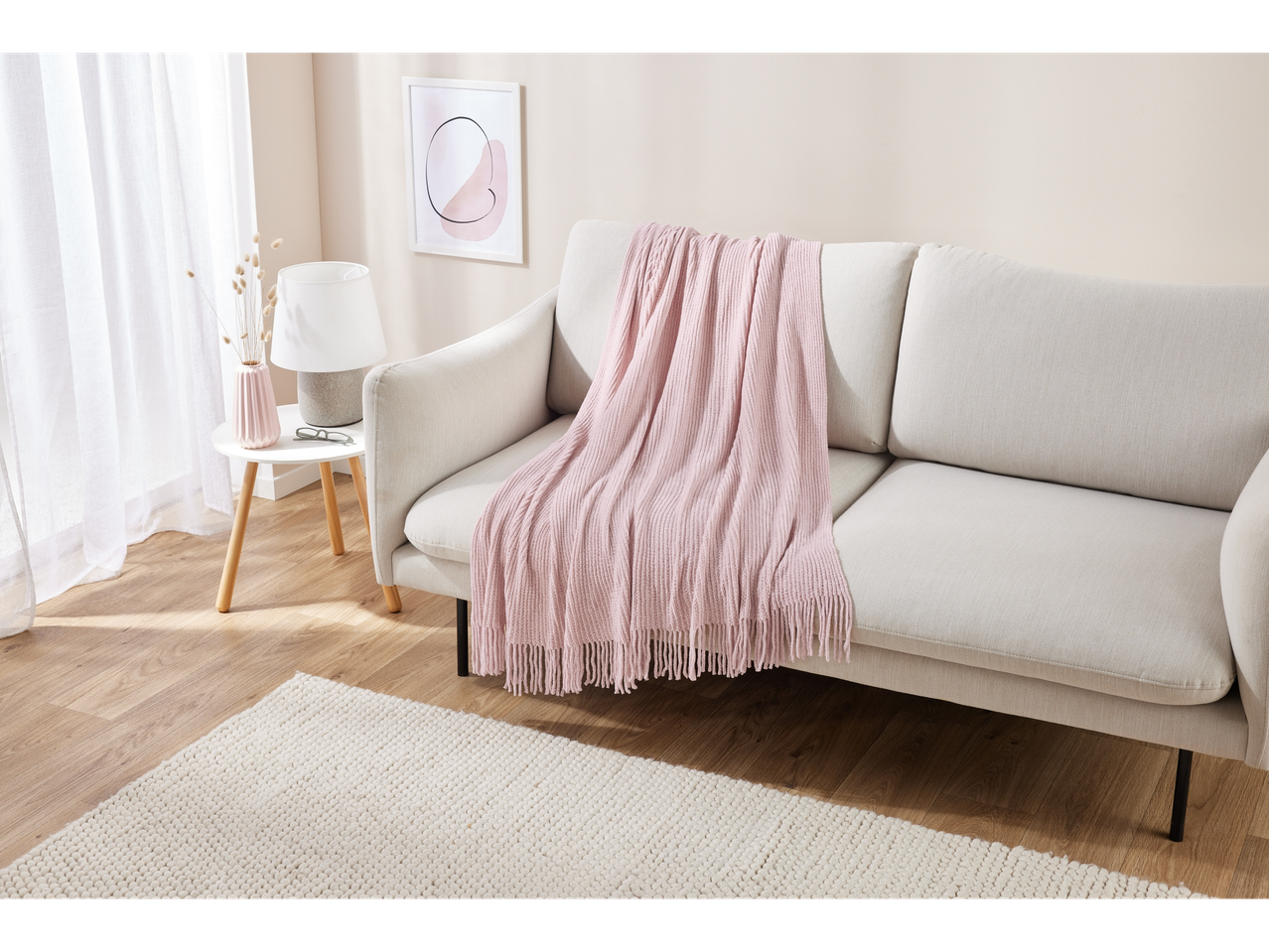 Uma sala de estar clara com um sofá bege, uma manta rosa e uma pequena mesa lateral.
