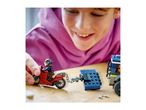 Smiling child playing with toy motorcycle and police truck on a wooden table.
