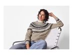 A smiling woman in a patterned knit sweater and jeans sits in a white chair.