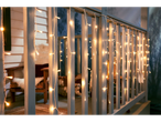 Porch railing with warm white icicle string lights, cozy outdoor seating in background.