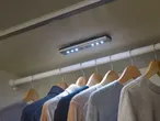 Φωτιστικό LED με αισθητήρα κίνησης τοποθετημένο σε ντουλάπα με ρούχα κρεμασμένα σε κρεμάστρες.