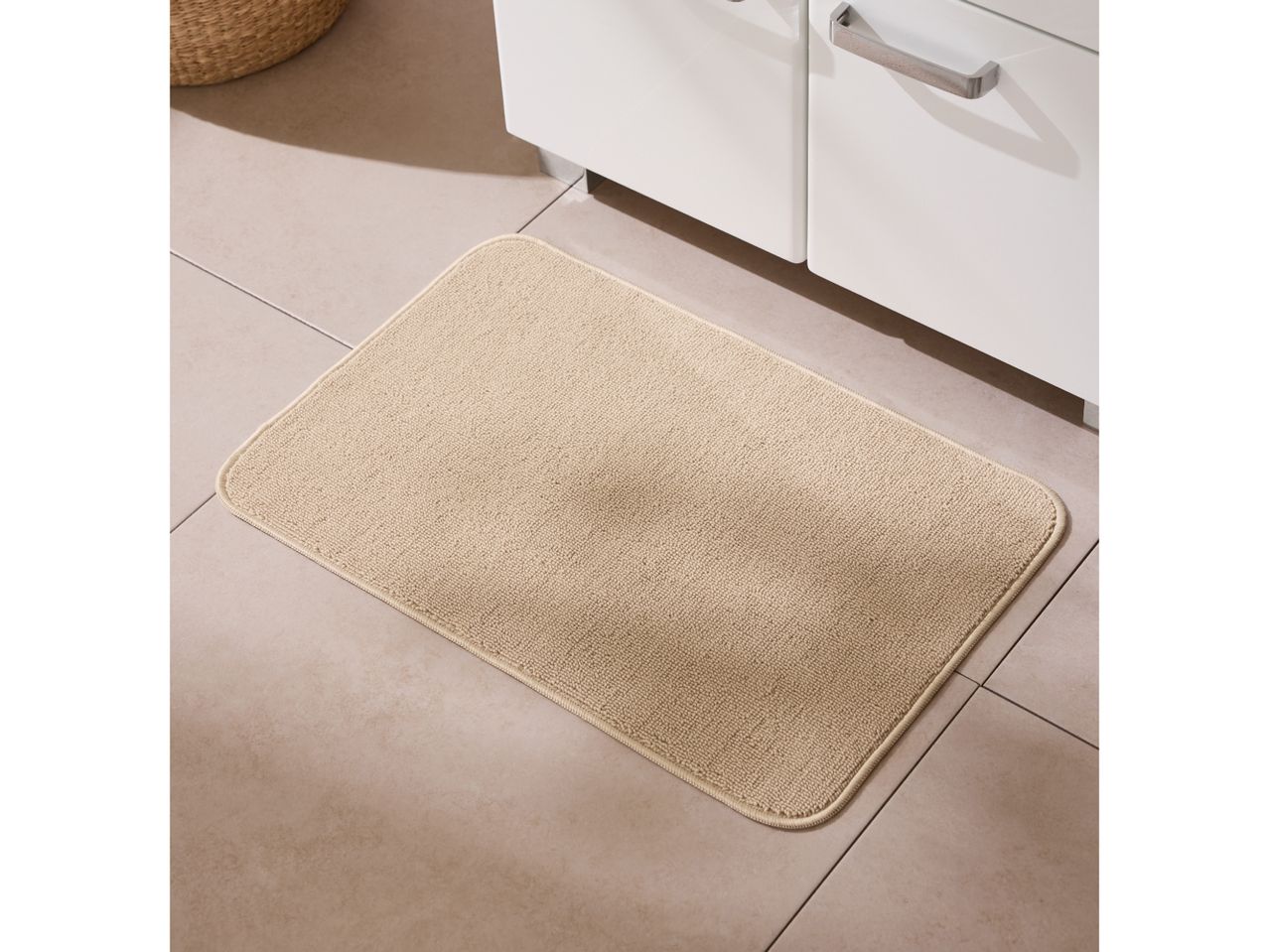 Beige bath mat on tiled floor in front of a white bathroom cabinet.