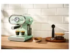 A mint green SilverCrest espresso machine brewing coffee into two glasses on a wooden counter.