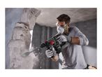 Man in safety gear using a cordless rotary hammer drill to break through a concrete wall.