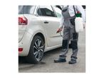 Person in overalls spraying a car tire with a pressure sprayer.