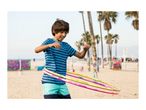 A boy in a blue striped t-shirt and swim shorts hula hooping on a sandy beach.