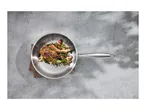 Stainless steel frying pan with a cooked pork chop, mushrooms, and herbs on a concrete surface.