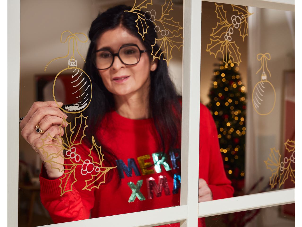 Woman decorating a window with crelando® Markers, drawing Christmas baubles and holly.