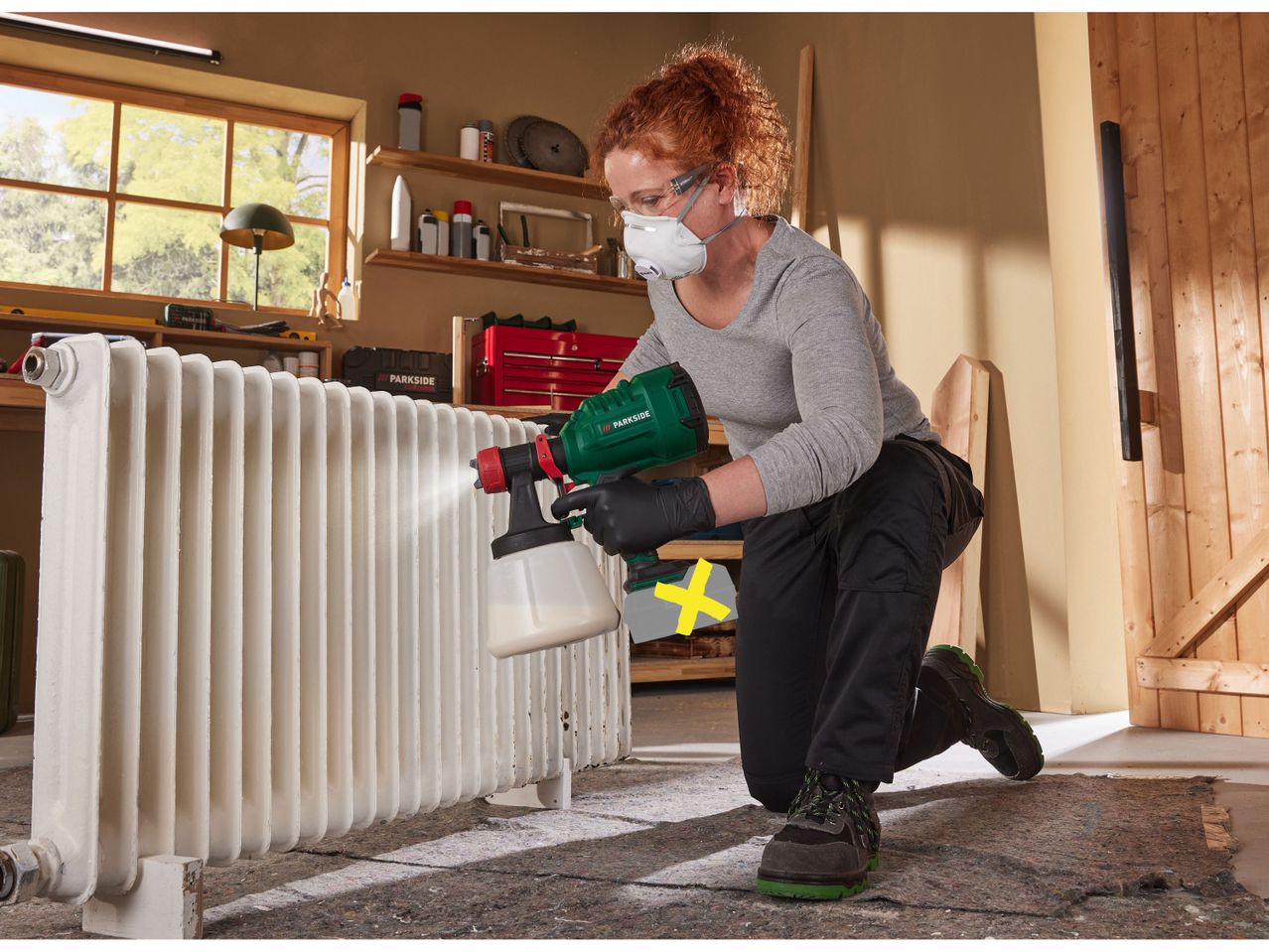 A woman uses a Parkside paint sprayer to paint a radiator in a workshop.