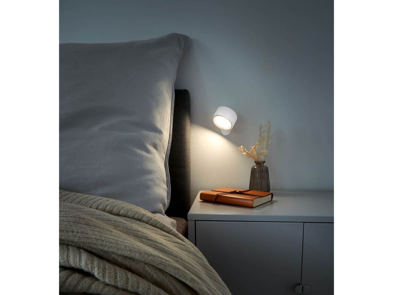 A cozy bedroom scene with a bed, nightstand, and a wall-mounted reading light.