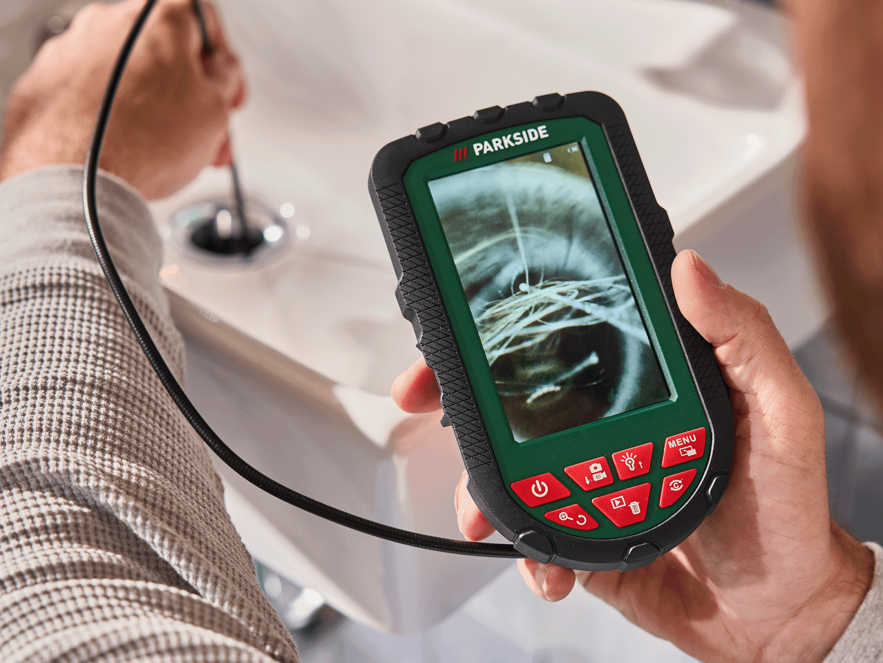 Moški uporablja endoskopsko kamero za pregled odtoka umivalnika, na zaslonu je vidna notranjost cevi.