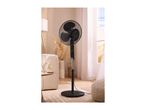 Black pedestal fan in a living room with a sofa, side table, and window.