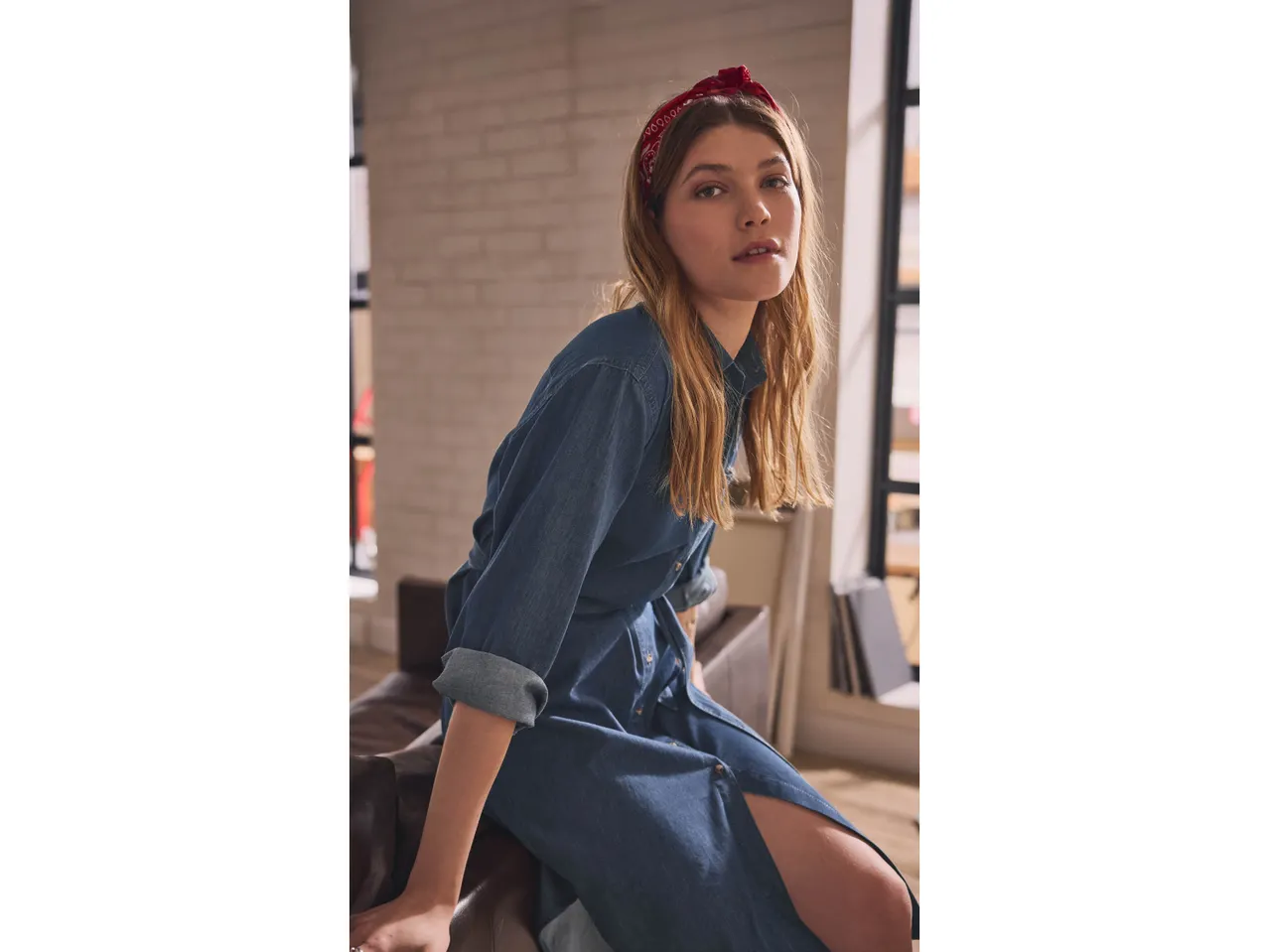 Donna con abito chemisier in denim blu e bandana rossa seduta su una poltrona in pelle.