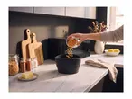 Person pouring popcorn kernels into a black bowl on a kitchen counter with a microwave.