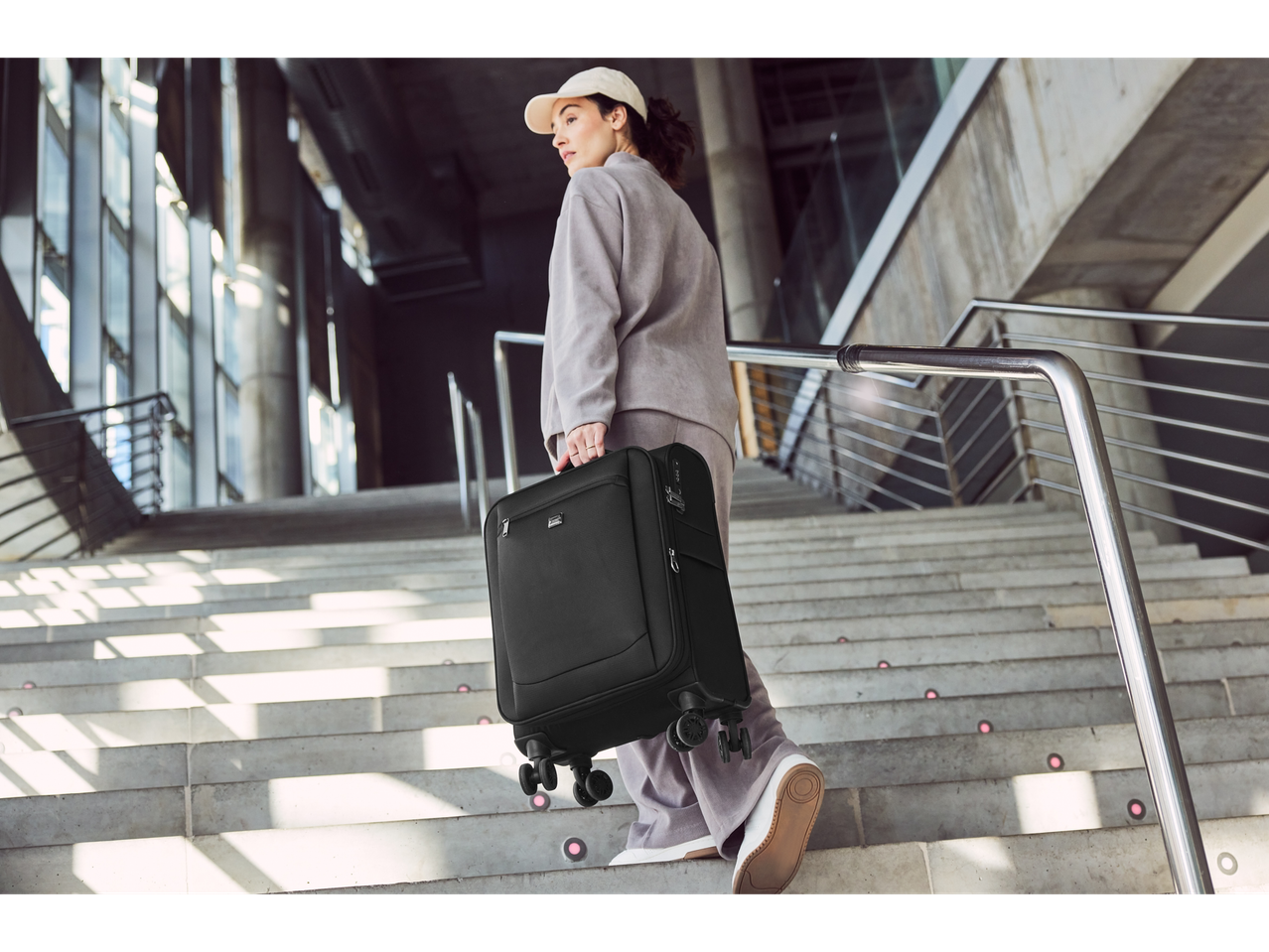 A woman carries a black Samsonite suitcase up a staircase.