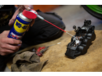 Um homem limpa uma pinça de freio com WD-40, com ferramentas e um pano por perto.