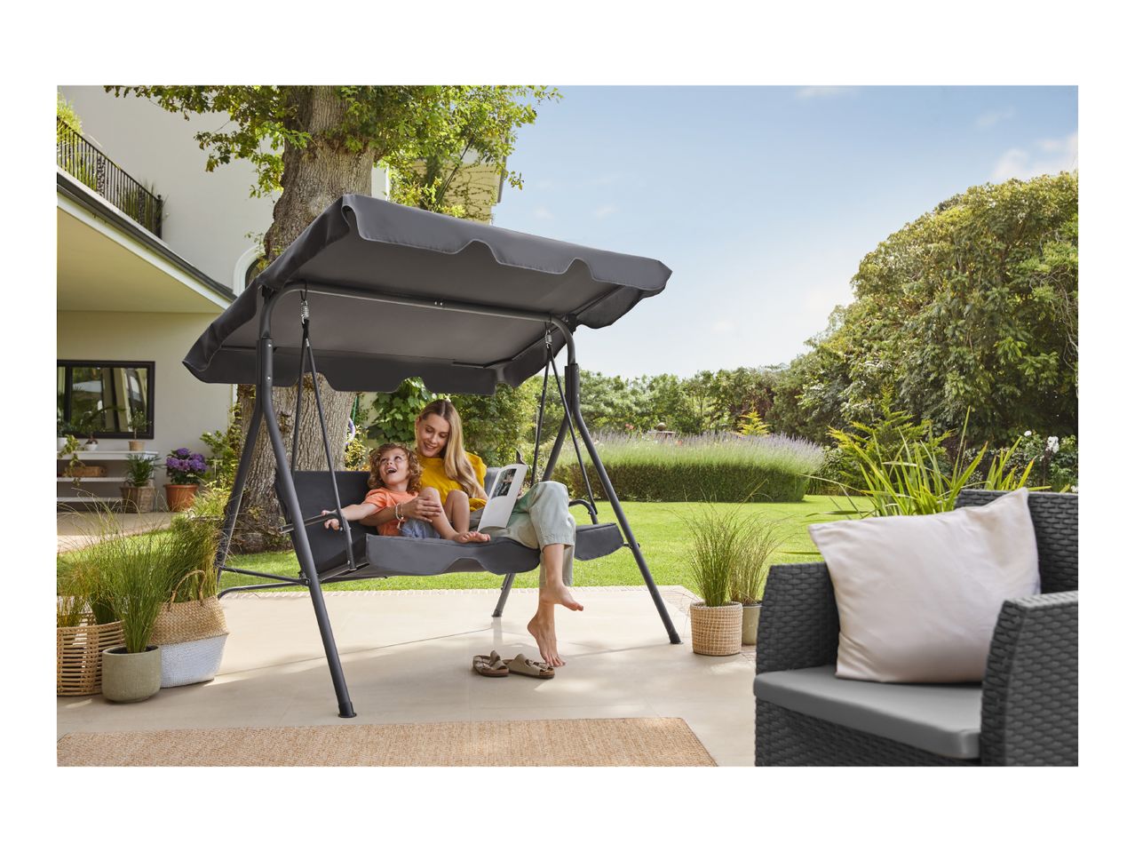 Mother and child on a garden swing seat with canopy, surrounded by garden furniture.