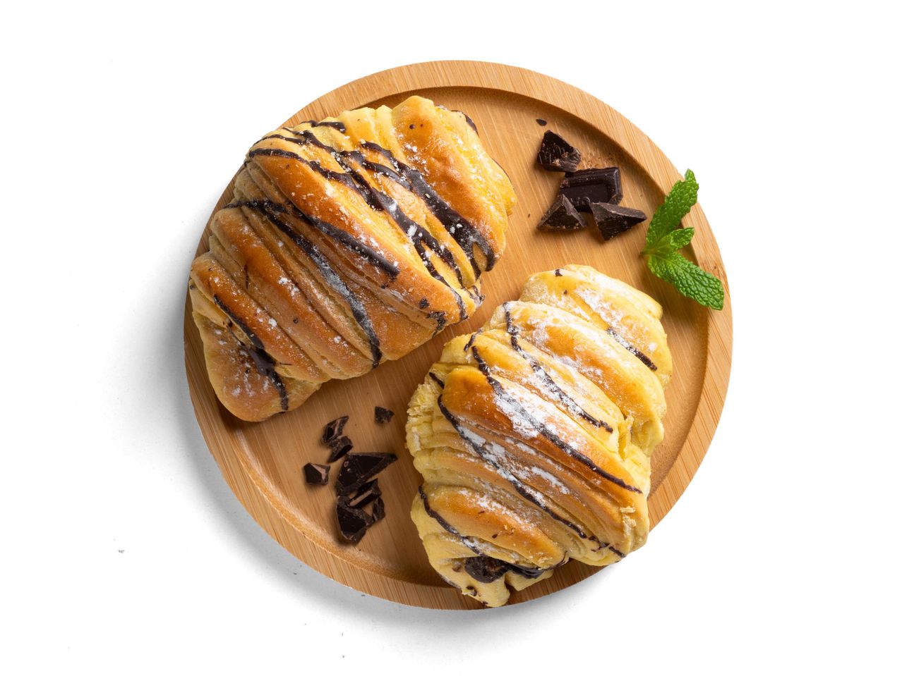 Két csokoládés croissant porcukorral, csokoládédarabokkal és mentával egy fa tálcán.