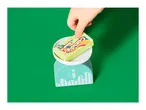 Child's hand placing a toy candy box on a toy kitchen scale.