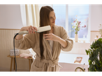 Woman in a bathrobe using a Cien BEAUTY Premium Hair Straightener on her wet hair in a bathroom.