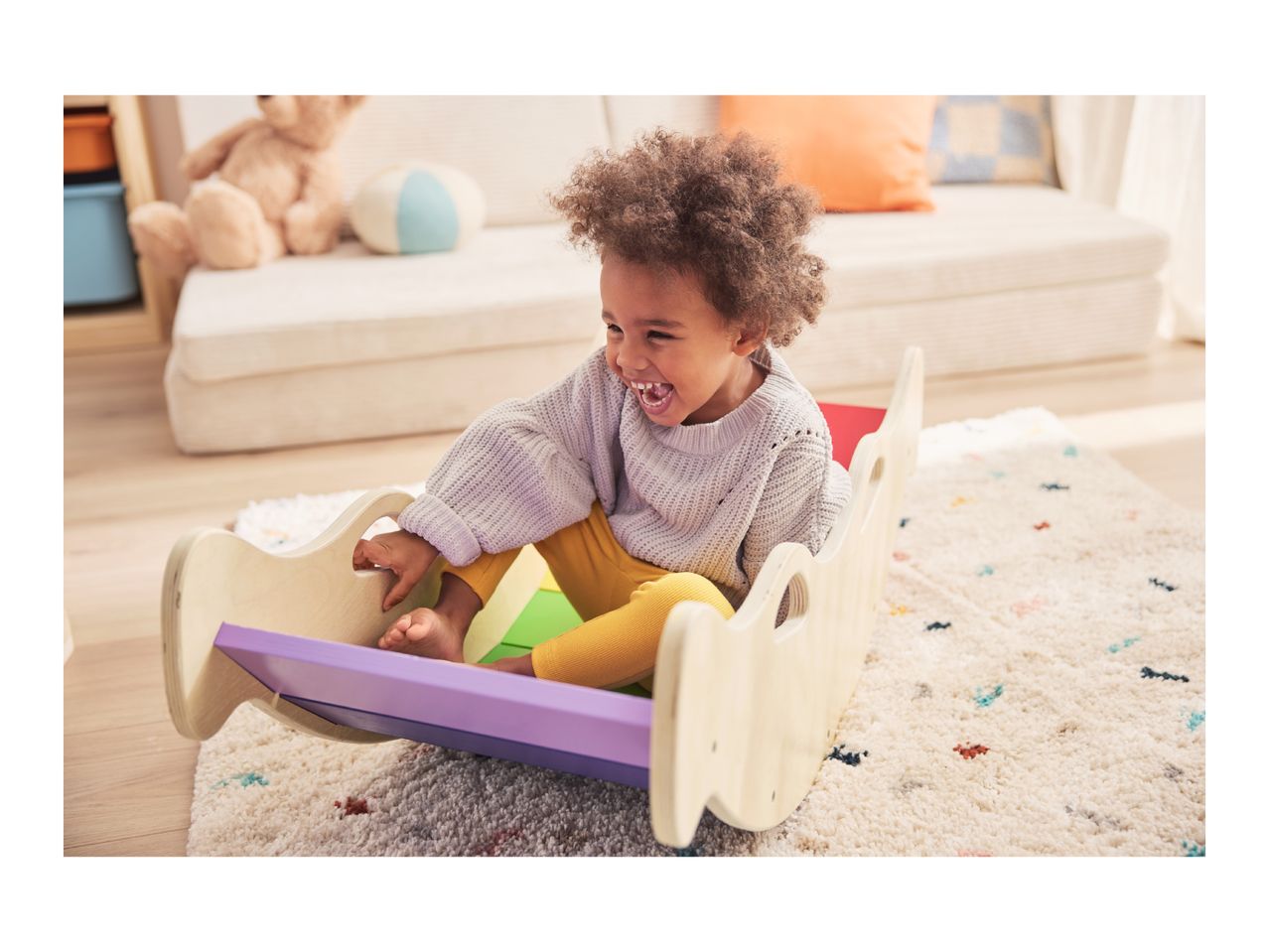 Happy child playing in a wooden rocker in a living room.