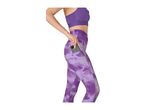 Woman in purple sports bra and patterned leggings putting a phone into a side pocket.