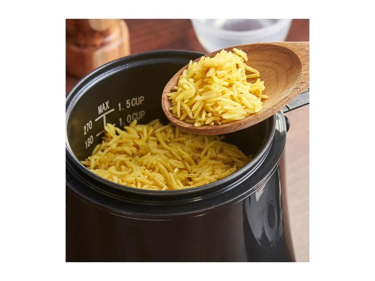 Cooked rice being scooped from a rice cooker with a wooden spoon.