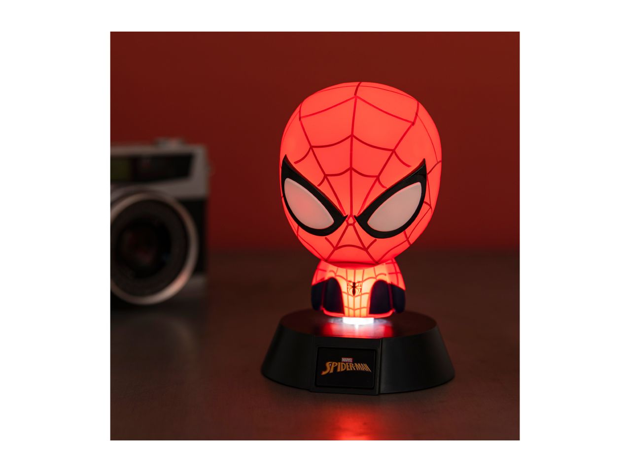 A glowing red superhero character lamp on a dark base, with a camera in the background.