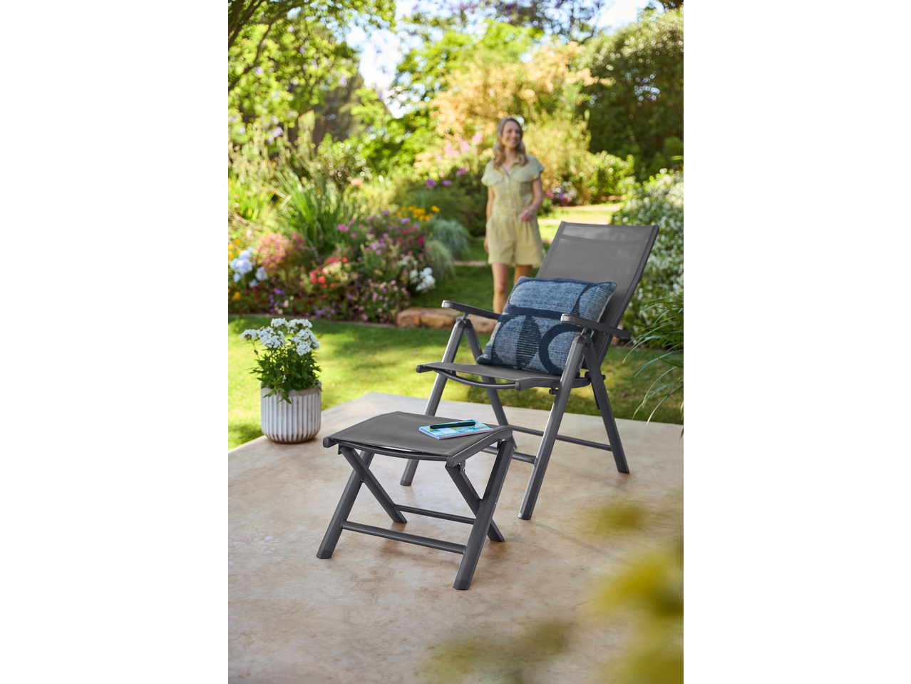 Grey garden chair and footstool with a cushion, notebook, and pen on a patio.