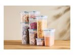 A variety of clear plastic food storage containers filled with dry goods on a wooden surface.