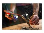 Person spraying lubricant on a metal tool held by locking pliers on a wooden surface.