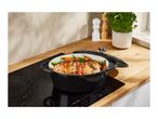 A black cast iron pot with a roasted chicken and vegetables on an induction cooktop.