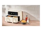 Cream air fryer with two baskets, one with chicken, one with fries, on a wooden counter.