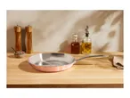 Copper frying pan on a wooden counter with salt and pepper grinders, and oil bottles.
