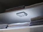 Φωτιστικό LED τοποθετημένο σε ράφι ντουλάπας, φωτίζοντας διπλωμένα ρούχα.