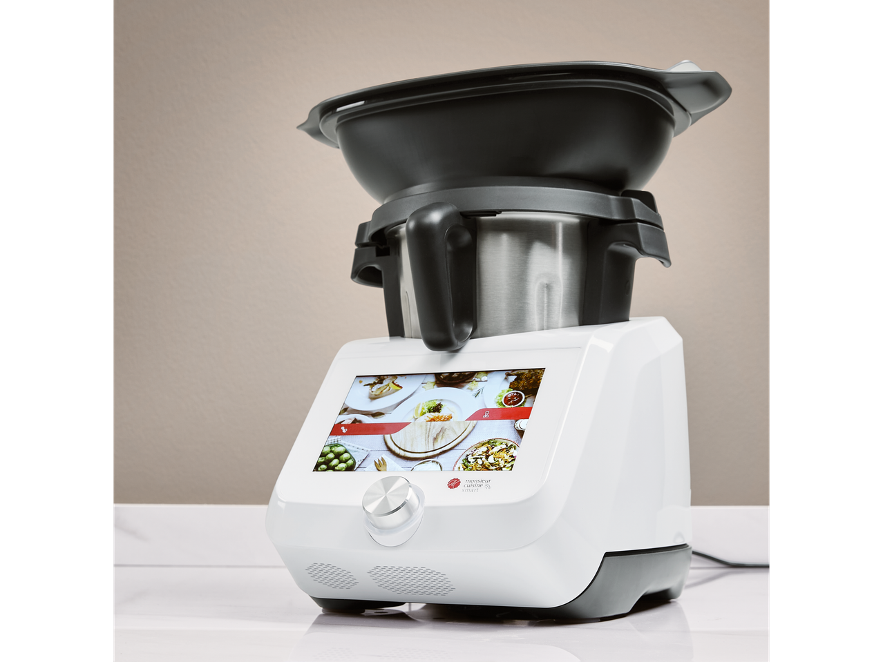A white and black Monsieur Cuisine Smart food processor with a screen displaying food recipes.