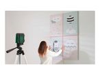 A woman uses a laser level to align four decorative pictures on a wall.